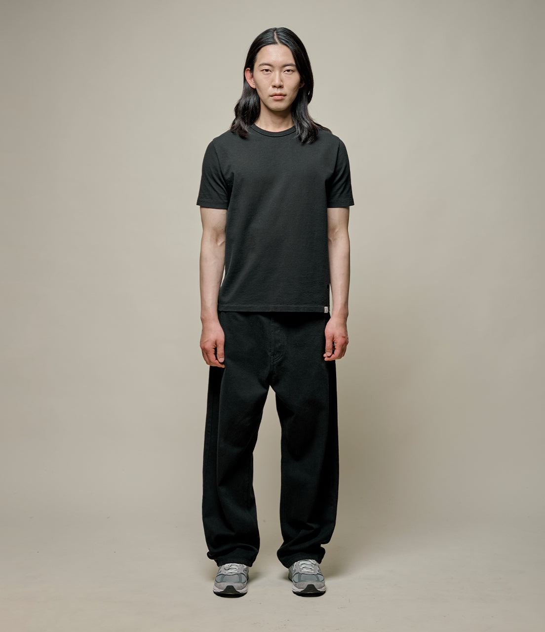 Person wearing a black t-shirt and black pants on a beige background
