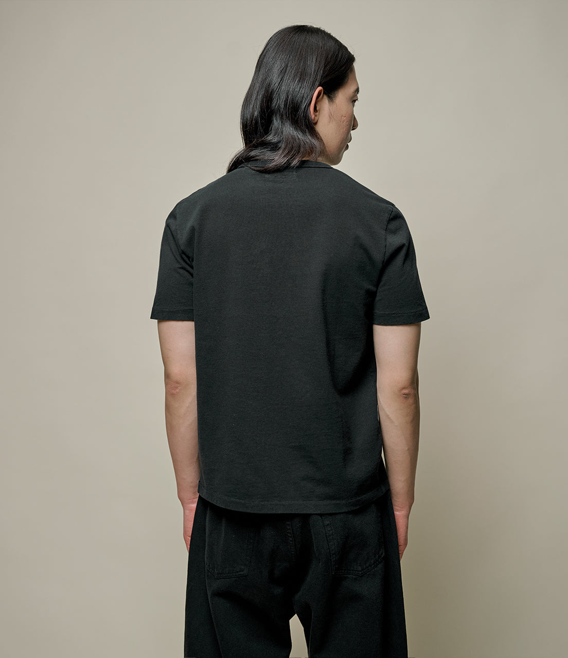 Person wearing a black t-shirt and pants against a beige background