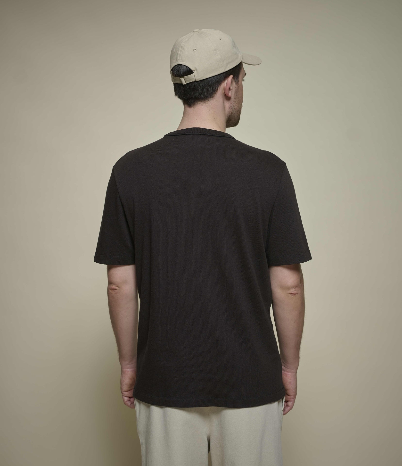 Man wearing a dark brown t-shirt and beige cap against a beige background