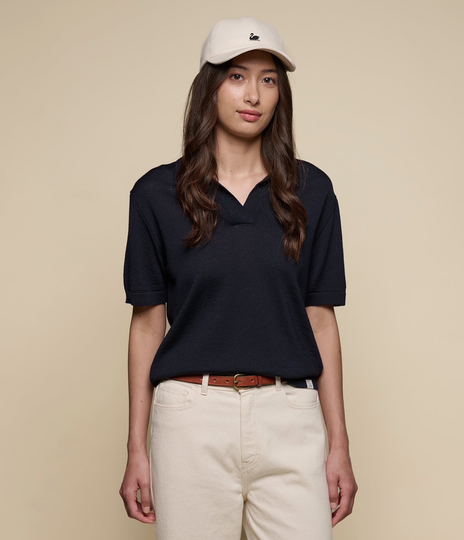 Woman wearing a dark navy knitted polo shirt and beige cap on a beige background
