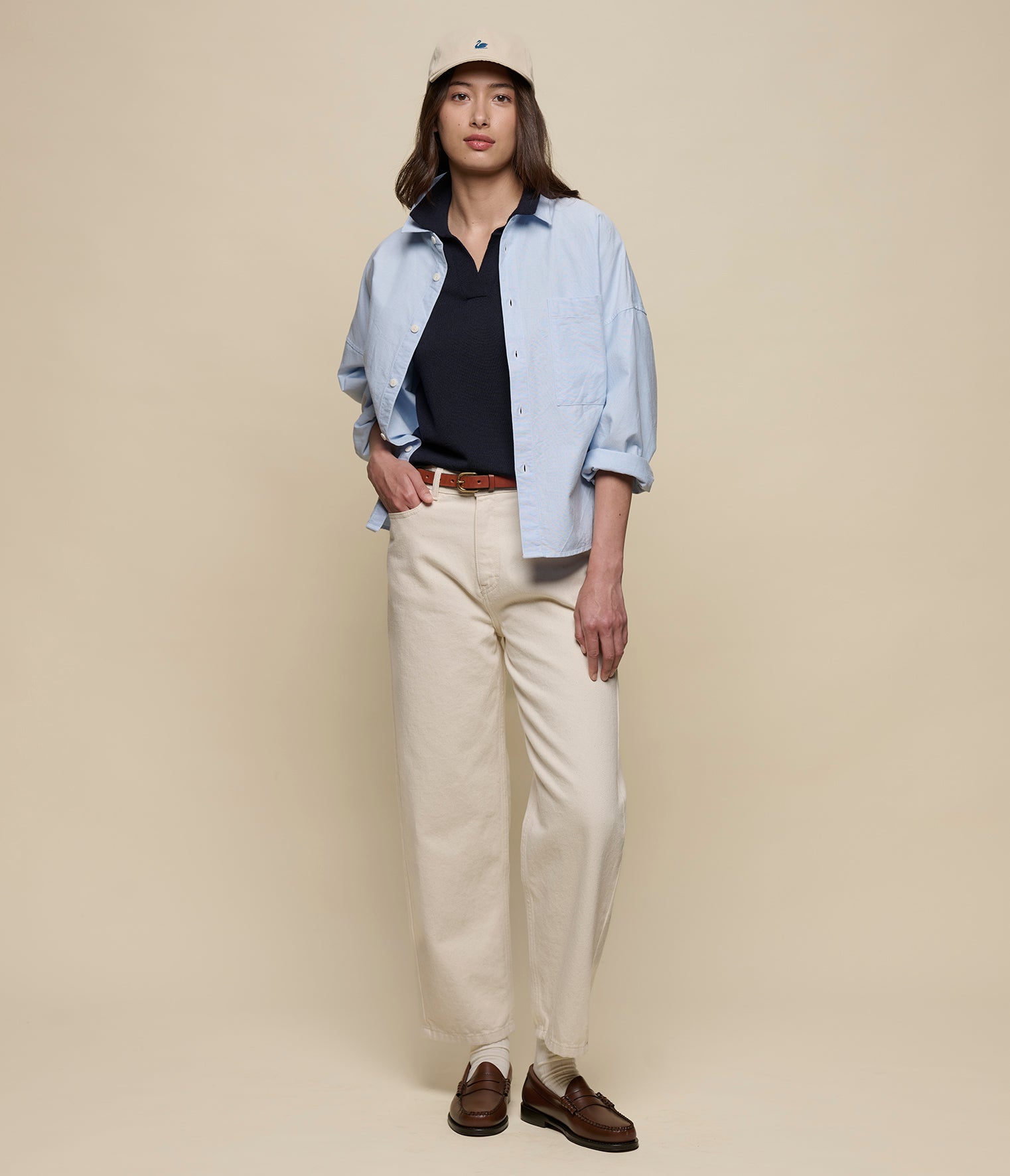 Person wearing a light blue oxford shirt, dark navy polo shirt, beige pants, and brown shoes against a beige background