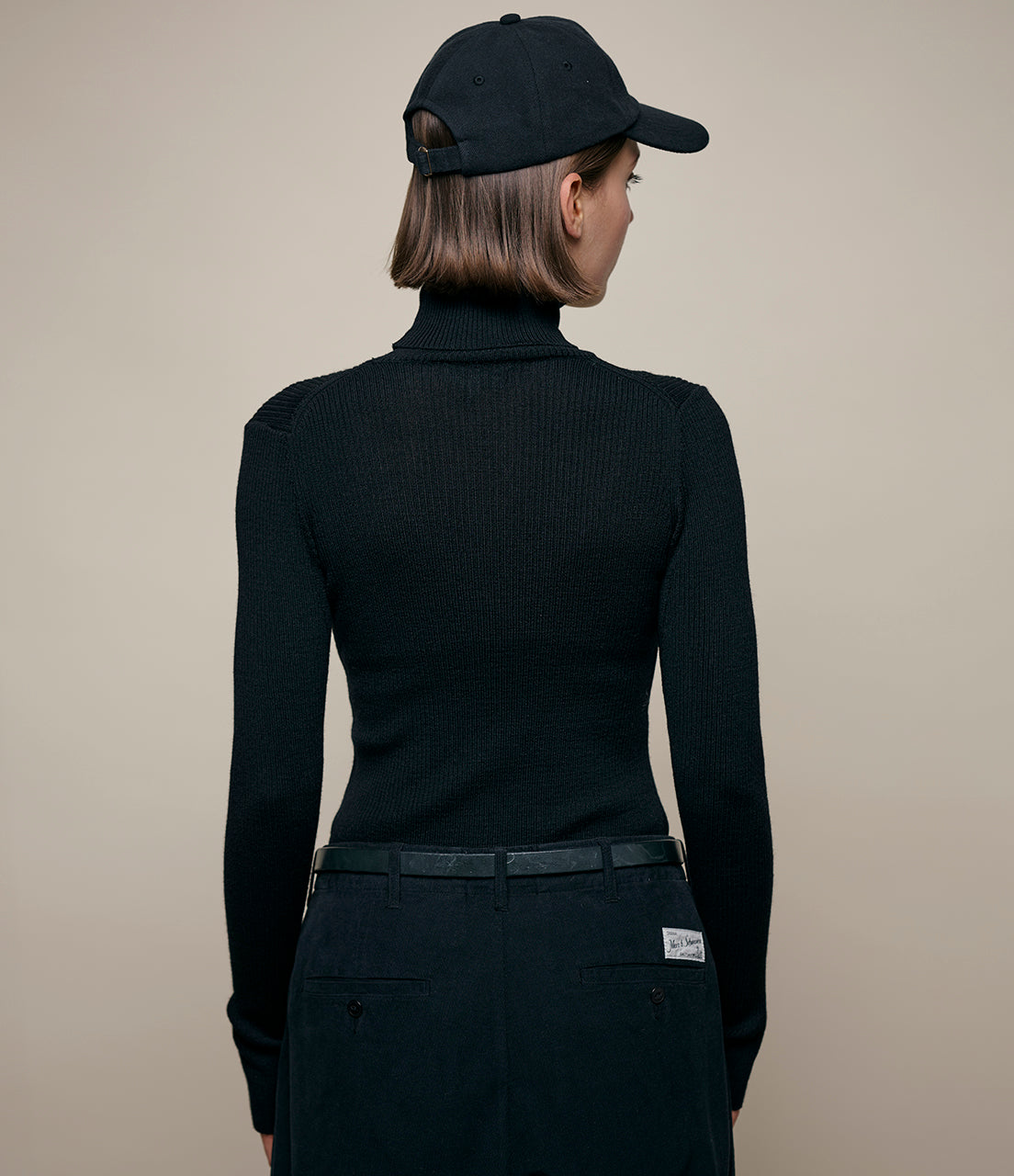 Person wearing a black turtleneck sweater and cap on a beige background
