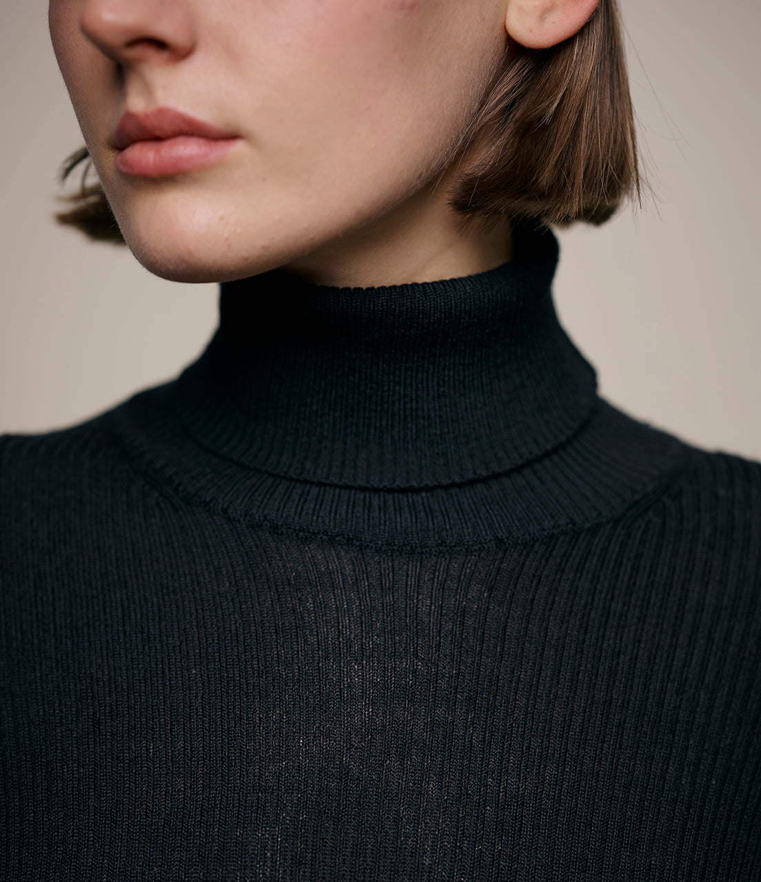 Close-up of a person wearing a black turtleneck sweater against a neutral background