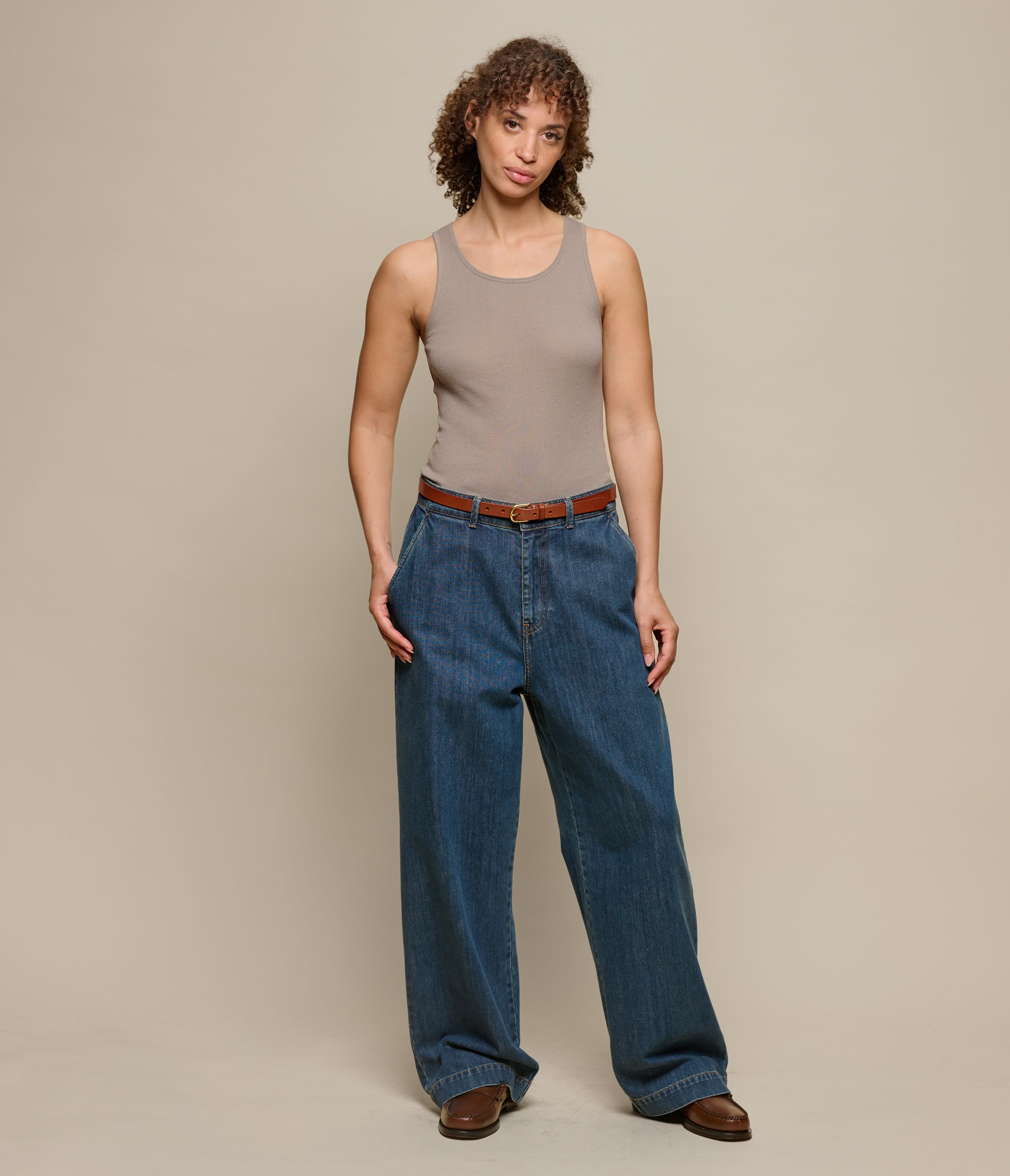 Woman wearing a brown ribbed tank top and blue jeans on a beige background