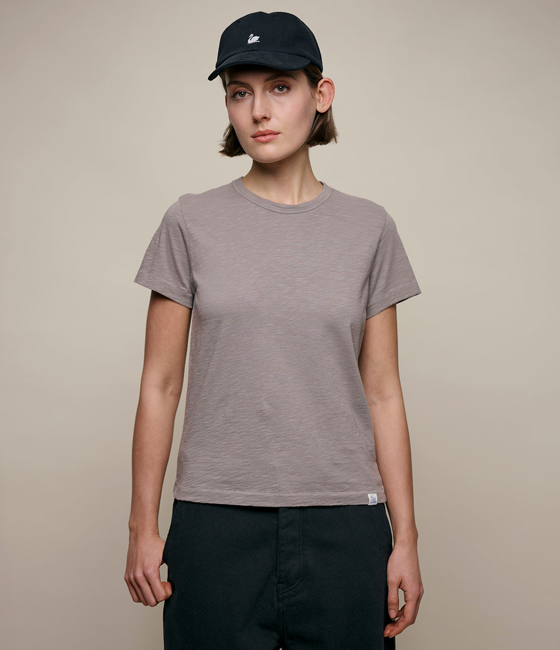 Person wearing a gray t-shirt and black cap on a beige background