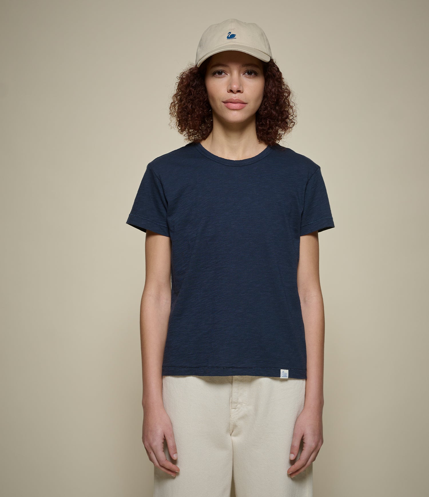 Person wearing a navy t-shirt and beige cap on a plain background
