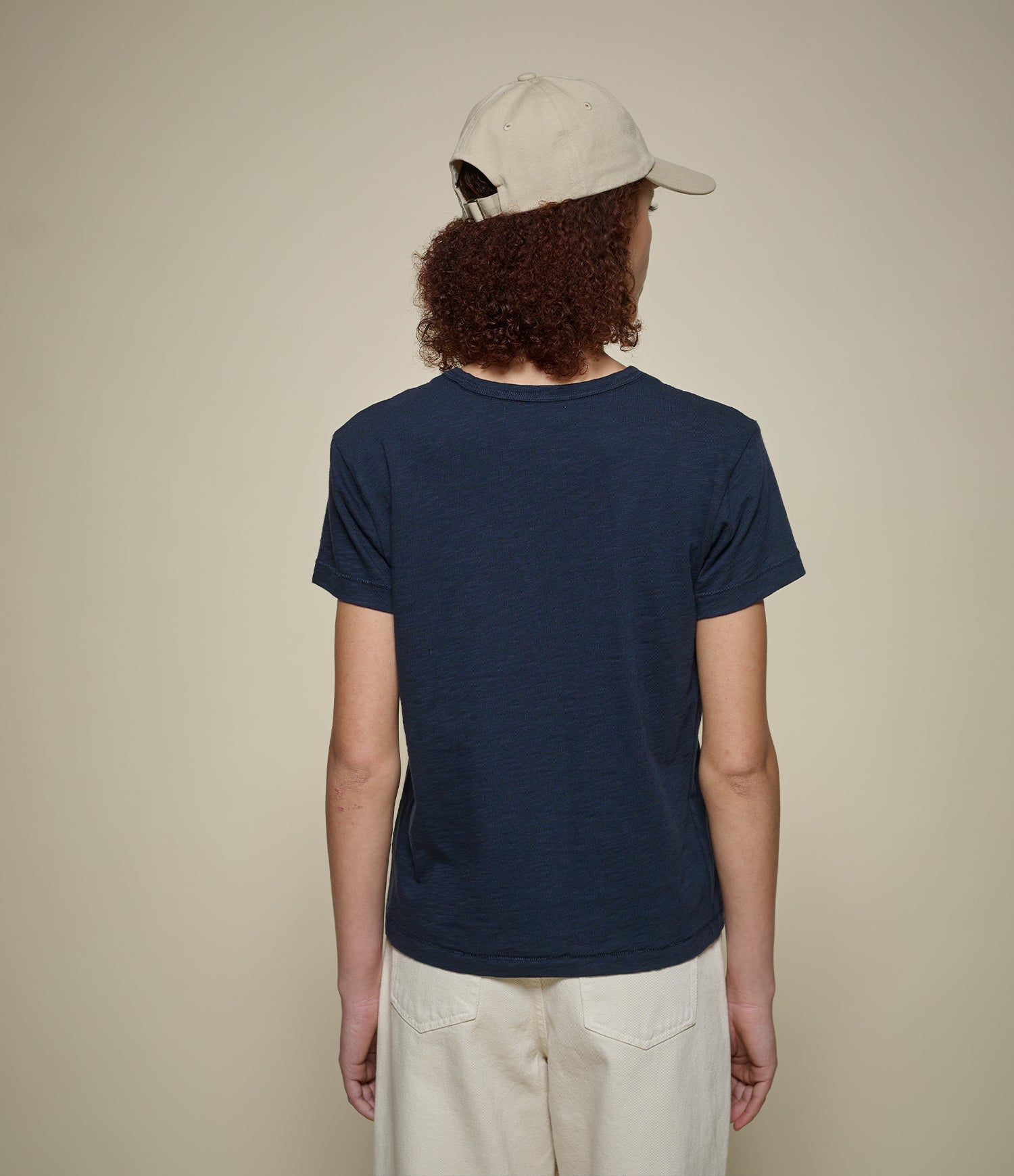 Person wearing a navy t-shirt and beige cap on a plain background