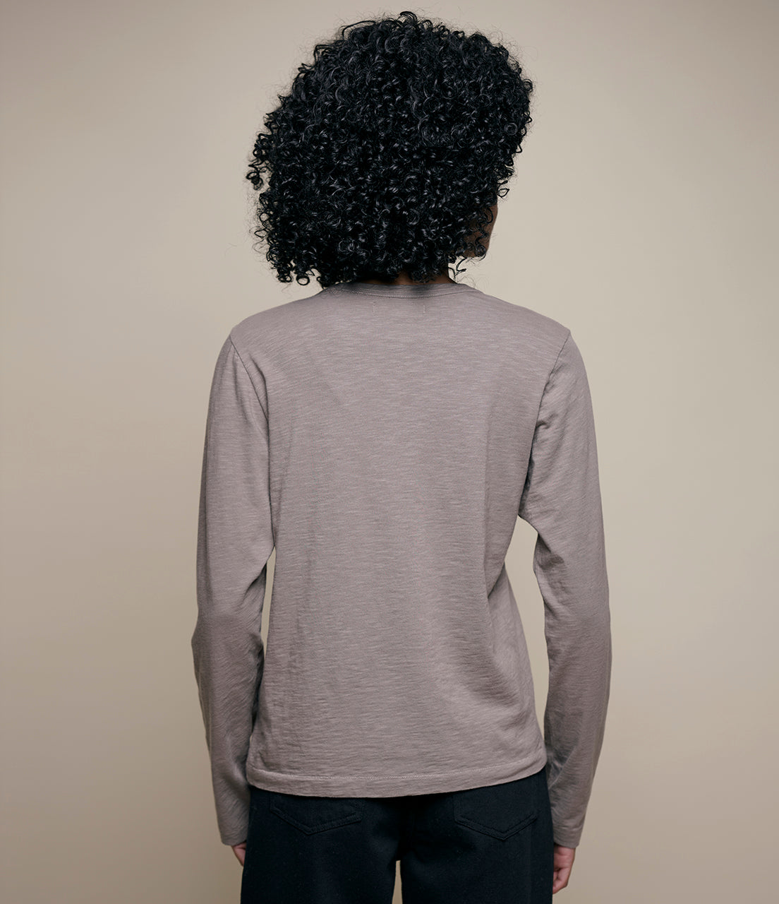 Person wearing a gray long-sleeve shirt against a beige background
