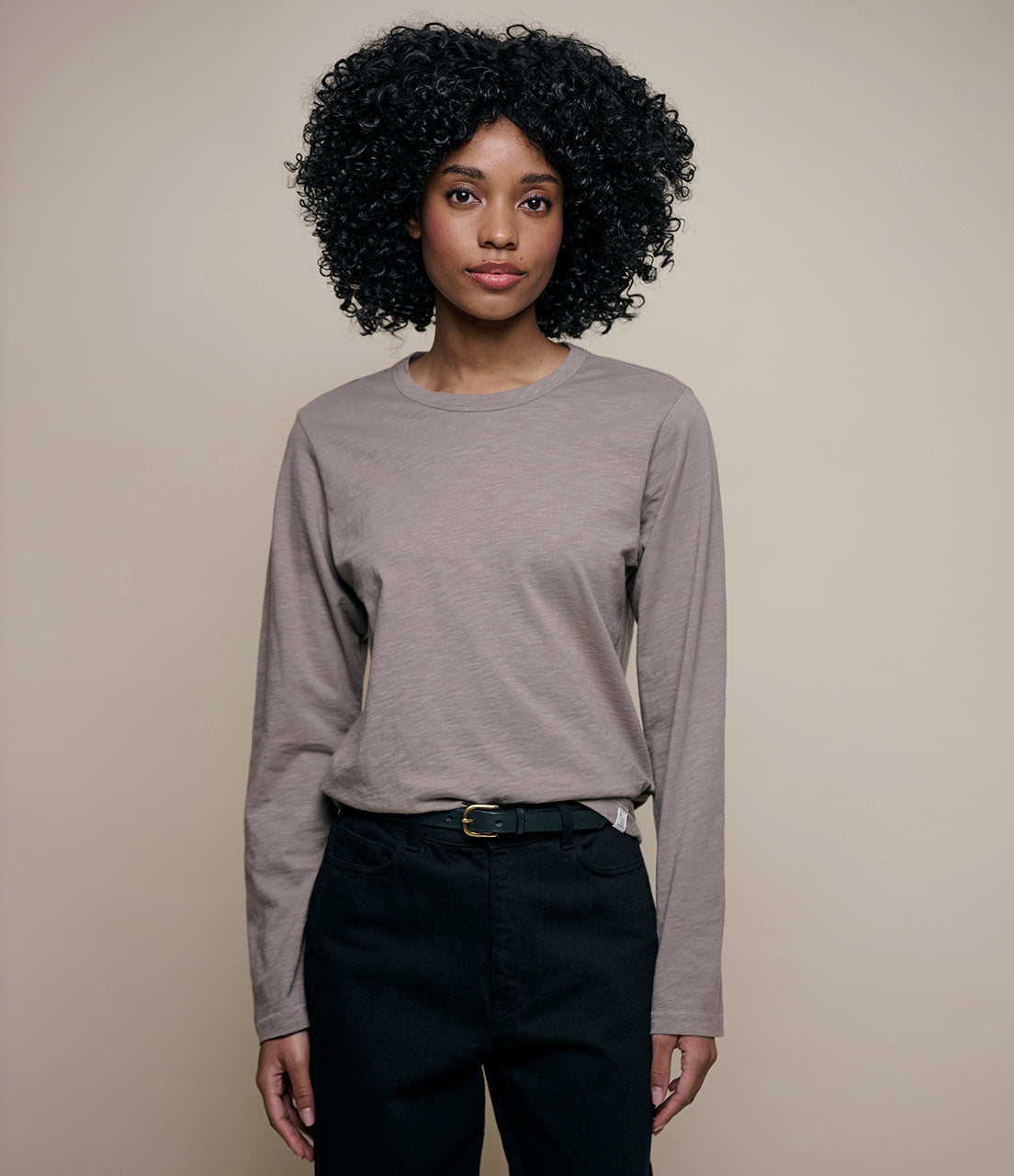 Woman wearing a gray long-sleeve shirt and black pants against a beige background