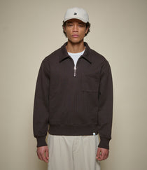 Man wearing a brown half-zip sweatshirt and beige cap against a beige background