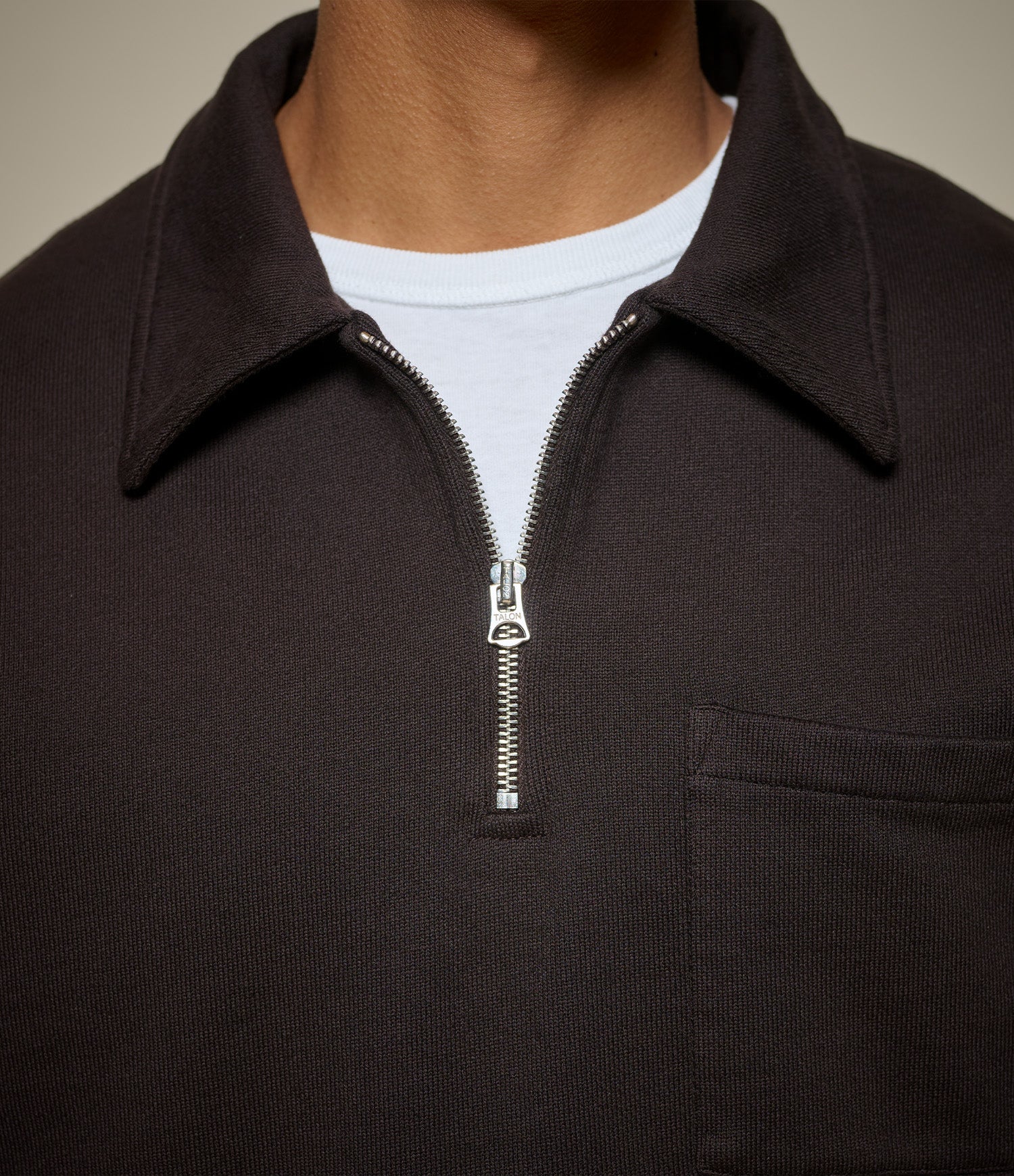 Close-up of a person wearing a dark brown zip-up shirt with a white shirt underneath.