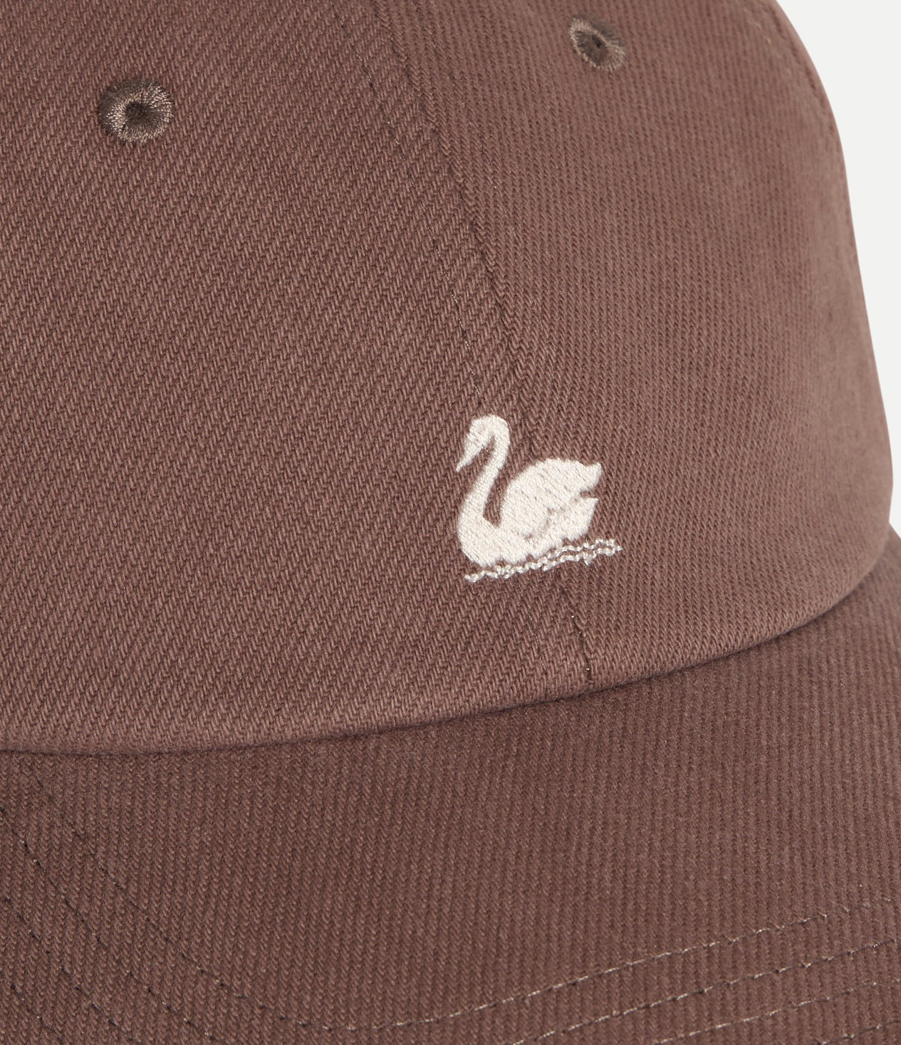 A close-up of a brown baseball cap featuring a small white embroidered swan logo on the front panel.